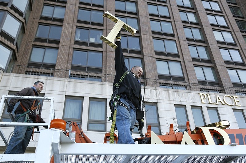 FILE- In this March 16, 2016 file photo, one of the workmen holds up the letter "T" as they remove the letters from a building formerly known as Trump Place in New York. Owners of the last of six luxury New York City condominiums that once displayed the president's name have voted to have name removed from the building. On Friday, Feb. 22, 2019, apartment owners got an email from the board of managers of a high-rise on Manhattan's west side confirming that "Trump Place" will disappear from the facade. (AP Photo/Seth Wenig, File)

