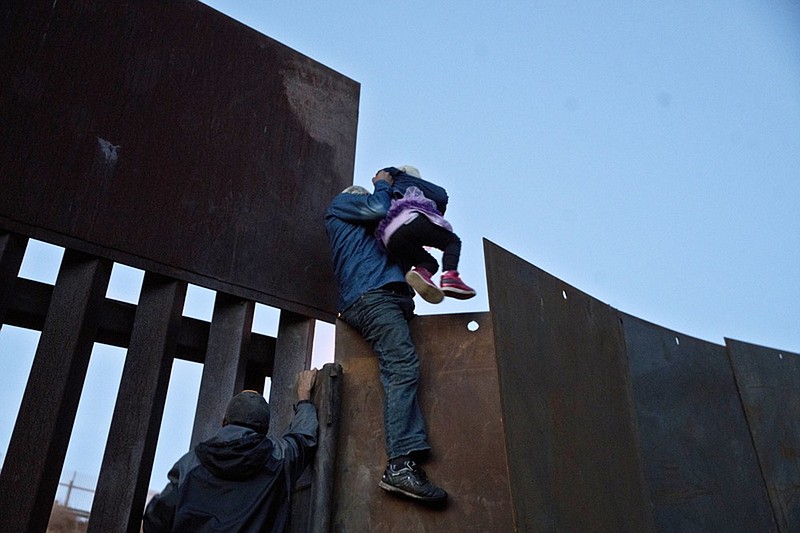 FILE - In this Dec. 2, 2018 file photo, a Honduran migrant helps a young girl cross to the American side of the border wall, in Tijuana, Mexico. A San Diego TV station says the U.S. government ran an operation to screen journalists, activists and others while investigating last year's migrant caravan from Mexico. KNSD-TV says documents leaked by a Homeland Security source show a January database listing at least 10 journalists, seven of them U.S. citizens, as warranting secondary screening at U.S. points of entry. (AP Photo/Ramon Espinosa, File)

