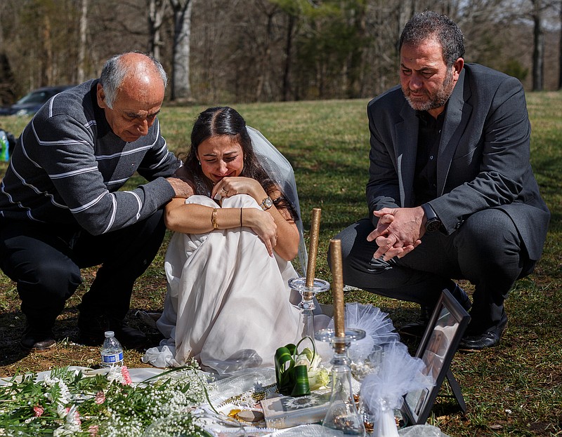 Clad in a wedding dress, Sara Baluch, center, mourns with her father Masoud Baluch, left, and her fiance's father Mohssen Sharifi while visiting the grave of her fiance, Mohammad Sharifi, on Sunday, March 10, 2019, the day after they were supposed to be married, at Harpeth Hills Memory Gardens in Nashville, Tenn. Sharifi, a UTC student, was shot and killed two weeks before their wedding by a man to whom he was trying to sell an Xbox.