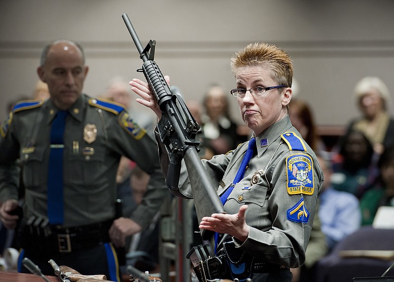 FILE - In this Jan. 28, 2013, file photo, firearms training unit Detective Barbara J. Mattson, of the Connecticut State Police, holds a Bushmaster AR-15 rifle, the same make and model used by Adam Lanza in the 2012 Sandy Hook School shooting, during a hearing at the Legislative Office Building in Hartford, Conn. A divided Connecticut Supreme Court ruled, Thursday, March 14, 2019, gun maker Remington can be sued over how it marketed the Bushmaster rifle used in the massacre. (AP Photo/Jessica Hill, File)