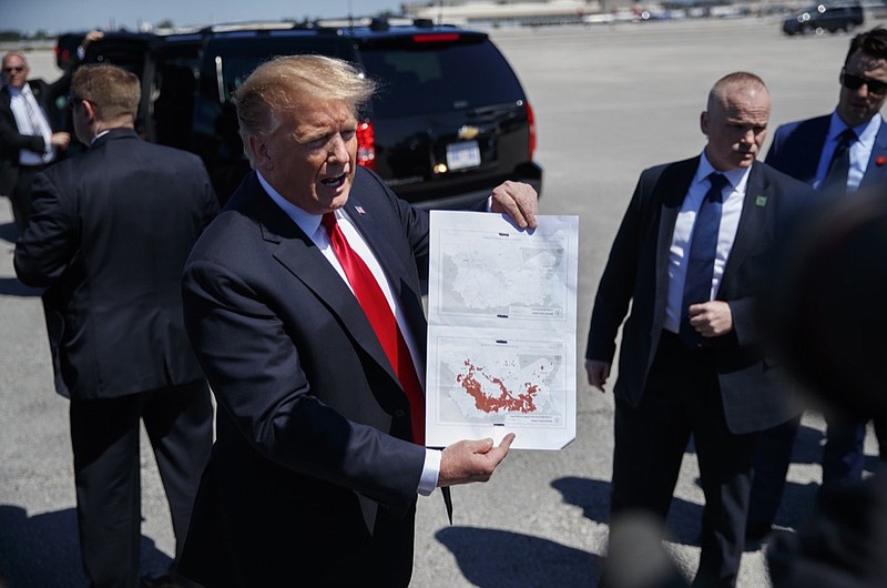 President Donald Trump holds a a copy of two maps of Syria as he arrives on Air Force One, Friday, March 22, 2019, at Palm Beach International Airport, in West Palm Beach, Fla. One map is awash in red shows IS controlled territory in Syria in November 2016. The other, without red, indicates that IS as of today no longer controls territory in Syria. (AP Photo/Carolyn Kaster)

