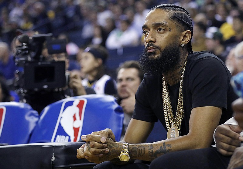 FILE - In this March 29, 2018, file photo, rapper Nipsey Hussle watches an NBA basketball game between the Golden State Warriors and the Milwaukee Bucks in Oakland, Calif. Grammy-nominated and widely respected West Coast rapper Nipsey Hussle has been shot and killed outside his Los Angeles clothing store, Los Angeles Mayor Eric Garcetti said Sunday, March 31, 2019. He was 33. (AP Photo/Marcio Jose Sanchez, File)


