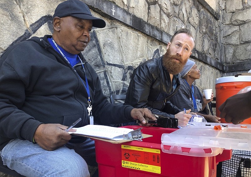 In this March 20, 2019 photo, Harry Ethridge, client services manager at the Atlanta Harm Reduction Coalition, and Jonathan Spuhler, an outreach coordinator for Absolute Care and volunteer at AHRC, set up a needle exchange station for drug users to swap out used syringes for clean syringes on English Avenue, in Atlanta. (AP Photo/Sanya Mansoor)

