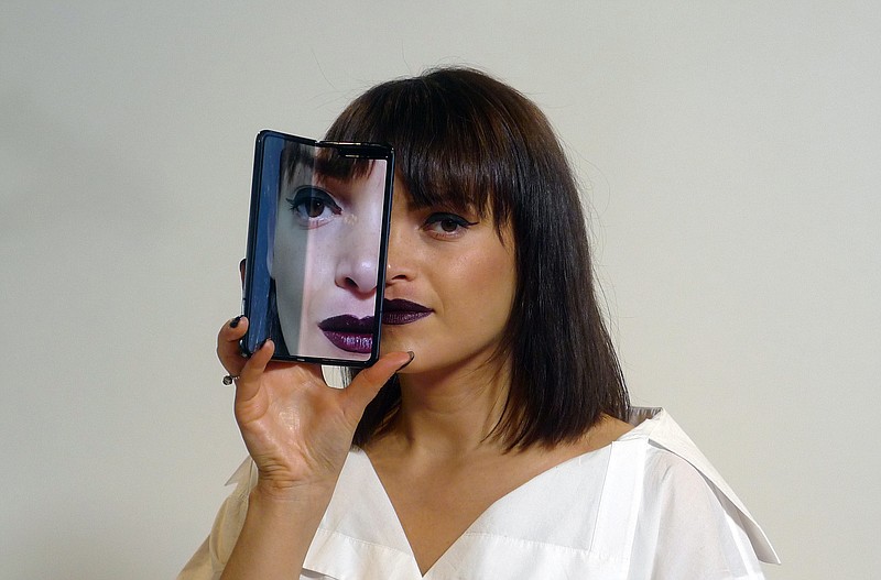 A model holds a Samsung Galaxy Fold smartphone to her face, during a media preview event in London, Tuesday April 16, 2019.  Samsung is hoping the innovation of smartphones with folding screens giving a large interactive space or smaller usual screen, reinvigorates the market. (AP Photo/Kelvin Chan)