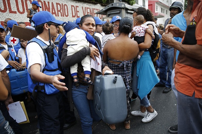 A woman with a child carries an empty container and water purification pills that came in the first aid shipment from the International Red Cross in Caracas, Venezuela, Tuesday, April 16, 2019. The first shipment of humanitarian aid from the Red Cross arrived in Venezuela on Tuesday, delivering medicine and supplies for needy patients in a country whose president has long denied the existence of a humanitarian crisis. (AP Photo/Ariana Cubillos)

