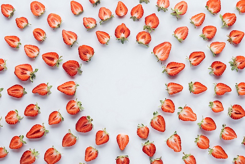 top view of round frame of ripe halved strawberries on white surface