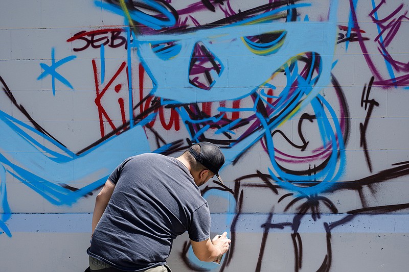 Artist Killamari paints a mural on a building along Oakland Avenue in Alton Park for the Burnin' Bridges Mural Jam on Friday, April 26, 2019, in Chattanooga, Tenn. 25 artists from across the country will be painting murals at the site through the weekend for the event, which was started by local artist SEVEN.