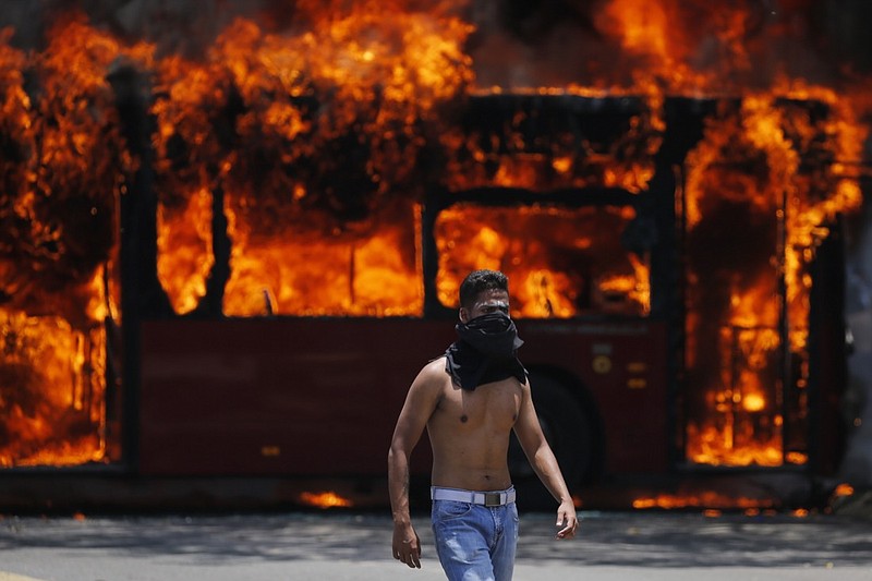 An anti-government protester walks near a bus that was set on fire by opponents of Venezuela's President Nicolas Maduro during clashes between rebel and loyalist soldiers in Caracas, Venezuela, Tuesday, April 30, 2019. Venezuelan opposition leader Juan Guaidó took to the streets with a small contingent of heavily armed troops early Tuesday in a bold and risky call for the military to rise up and oust Maduro. (AP Photo/Fernando Llano)