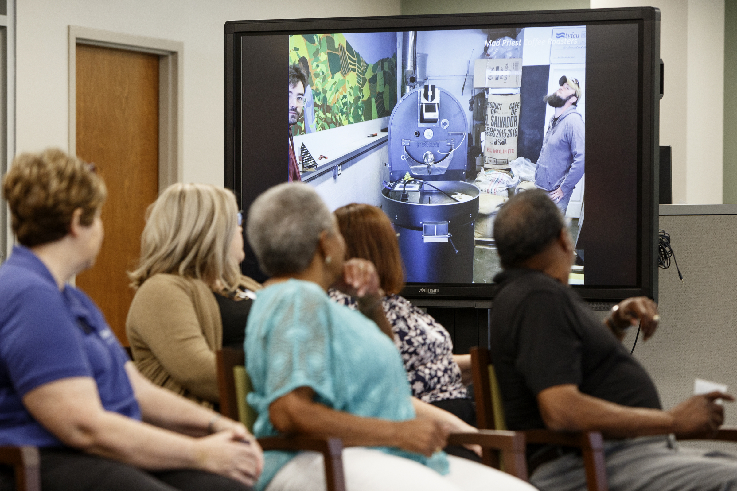 People look at a photo from Mad Priest Coffee, as they are moving their roaster, during the Idea Leap Grant kickoff breakfast at Tennessee Valley Federal Credit Union on Tuesday, May 7, 2019 in Chattanooga, Tenn. Mad Priest Coffee owner Michael Rice spoke during the kickoff and won the third place grant last year.