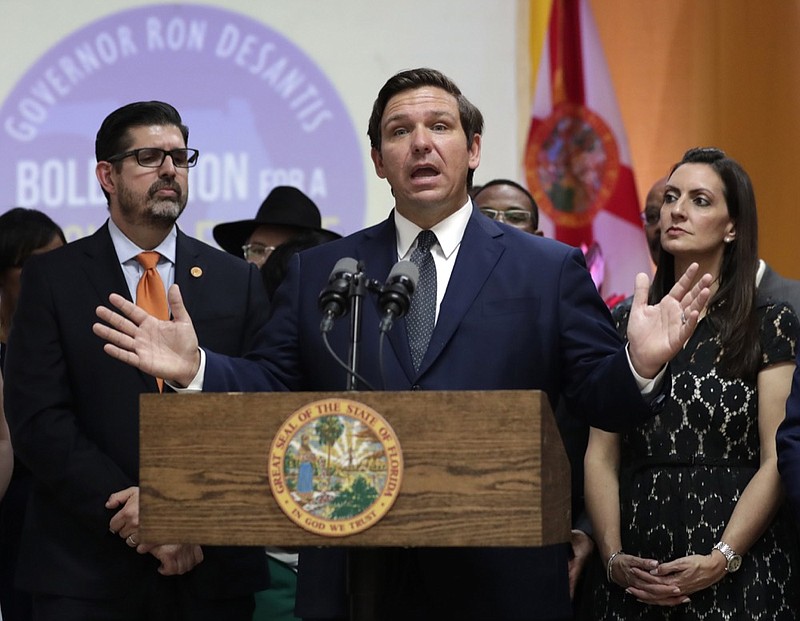 FILE- In this May 9, 2019 file photo. Florida Gov. Ron DeSantis, second from right, speaks during a bill signing ceremony at the William J. Kirlew Junior Academy, in Miami Gardens, Fla. Gov. DeSantis said Friday, May 17, 2019, that he plans to fight a federal plan to fly hundreds of immigrants from the Mexican border to two South Florida counties. He says he'll take his case to President Donald Trump. (AP Photo/Lynne Sladky, File)

