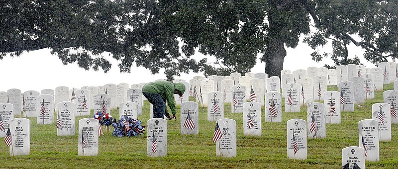 Bill Zimmerman, of Scottsboro Alabama, picks up debris from the grave of his father, William Zimmerman on Memorial Day.  The late Mr. Zimmerman served with the Army Air Corp and flew 35 missions over Europe in a B-17.  The heavy rain did not stop many people from visiting their loved ones in the National Cemetery on May 28, 2018.  