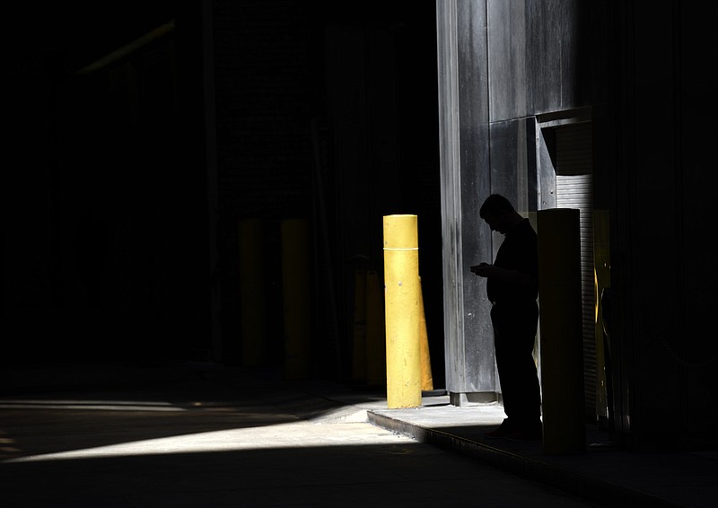 FILE - In this June 6, 2017, file photo a man checks his phone in an alley in downtown Chicago. The Consumer Financial Protection Bureau has proposed new rules to govern how third-party debt collectors contact borrowers. The rules are expected to accelerate the industry’s switch from insistent phone calls to emails and texts. Under the new rules, third-party debt collectors would only be able to call a delinquent borrower seven times a week, currently they can call as often as they want. And once they reach a borrower by phone, they’ll have to leave them alone for at least a week. (AP Photo/G-Jun Yam, File)