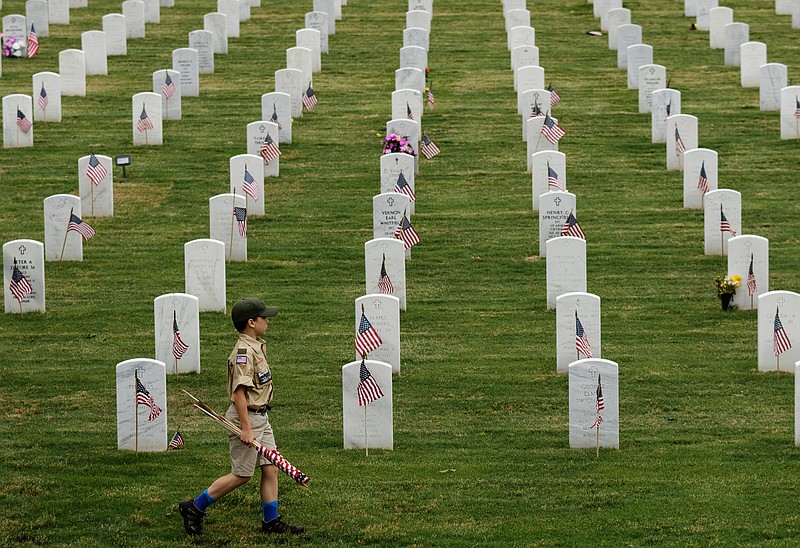 A Scout carries a bundle of flags past headstones at the Chattanooga National Cemetery after he and other Scouts placed more than 50,000 flags on the graves of veterans prior to Memorial Day in 2018.