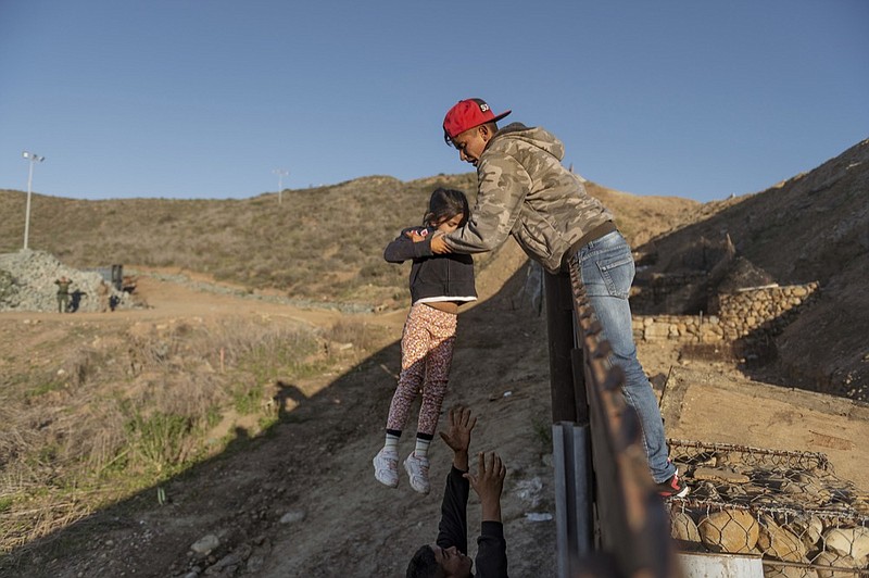 FILE - In this Jan. 3, 2019, file photo, a migrant from Honduras passes a child to her father after he jumped the border wall to get into the U.S. side to San Diego, Calif., from Tijuana, Mexico. A federal judge is expected to decide Friday, May 24 whether to block the White House from spending billions of dollars to build a wall on the Mexican border with money secured under President Donald Trump's declaration of a national emergency. (AP Photo/Daniel Ochoa de Olza, File)

