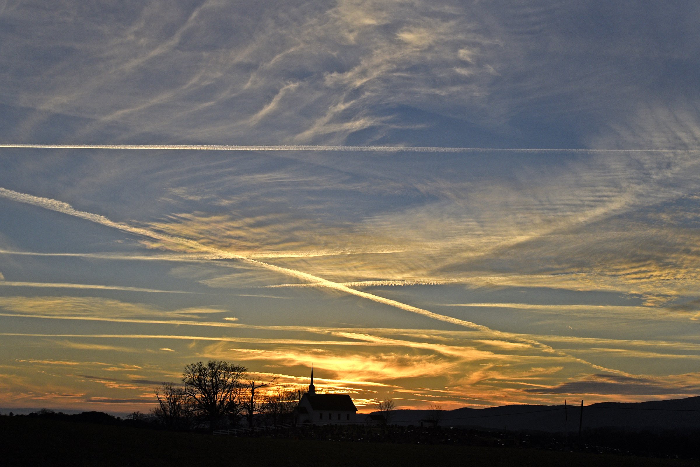 Clouds and contrails crisscross in the sky as the sun sets, recently, behind the Cumberland Plateau as Chapel Hill United Methodist Church and the surrounding trees stand in the foreground. The site has been a center for religious practice on the East Valley Road, east of Dunlap, in the Sequatchie Valley since 1851. The congregation now meets in a new, larger building north of Highway 127.
