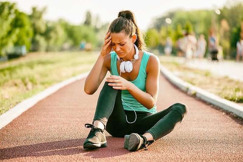 A young woman experiences a runner's headache while jogging on sunny day.