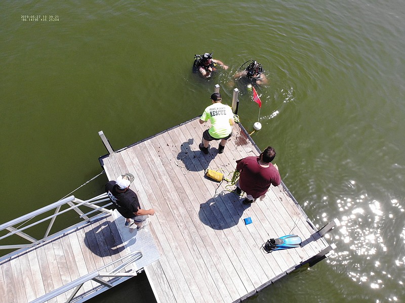 Franklin County Rescue Squad dive team members Jonathan Reed and A.J. Ladd, left to right in the water in this photo from the squad's drone, prepare to search for a retired veteran's wallet and keys as Kaleb Baxter, yellow shirt, and Alex Hiscock assist from the dock. An unnamed bystander watches at far left. Reed and Ladd found the wallet and keys along with a surprise discovery of a woman's purse that was returned to the owner as well.