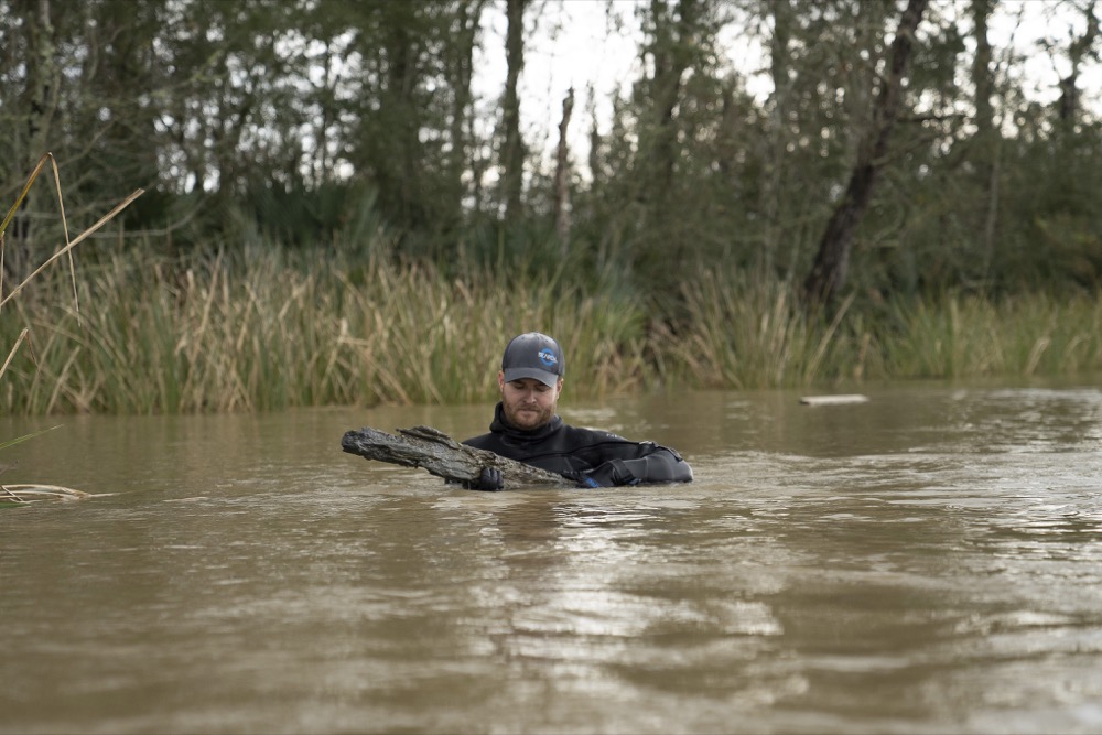 In this undated image released by SEARCH Inc., maritime archaeologist Kyle Lent examines a wooden plank from the hull of Clotilda, in delta waters north of Mobile Bay, Ala. Remains of the Gulf schooner Clotilda were identified and verified near Mobile after months of assessment, a statement by the Alabama Historical Commission said. (Daniel Fiore/SEARCH, Inc. via AP)