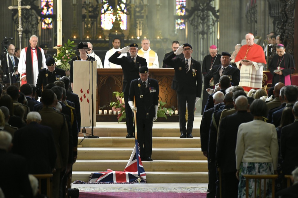 Bishop Jean-Claude Boulanger, right, looks at veterans lowering the Union Jack as they pay their respect during a ceremony at the Cathedral of Bayeux, Normandy, Thursday June 6, 2019, as part of D-Day commemorations marking the 75th anniversary of the World War II Allied landings in Normandy. (Bertrand Guay/ POOL via AP)
