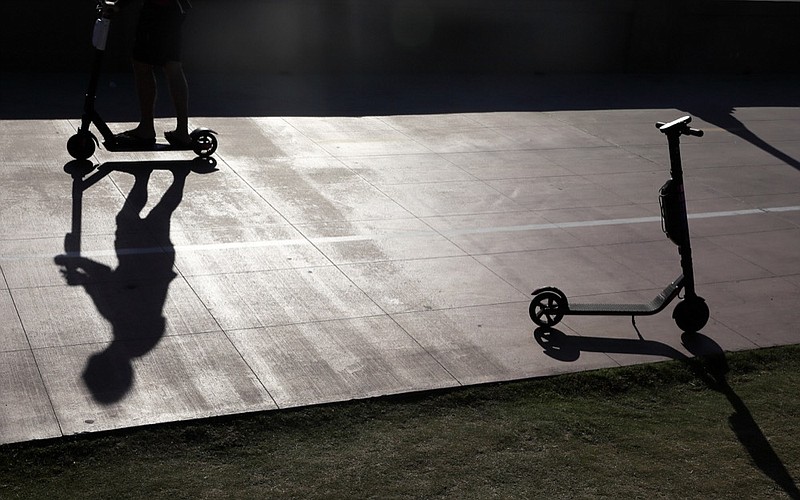 FILE - In this May 28, 2019, file photo, a man on a scooter passes a parked scooter along the Mission Beach boardwalk in San Diego. As electric scooters have rolled into more than 100 cities worldwide, many of the people riding them have ended up in the emergency room with serious injuries. Others have been killed.  (AP Photo/Gregory Bull, File)