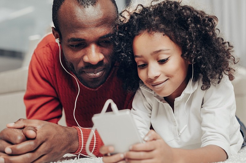 Content father and daughter listening to the music on smartphone while lying on the soft floor
music tile parenting tile parent headphones earbuds / Getty Images