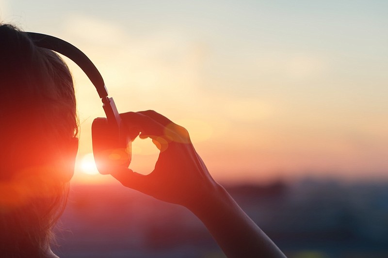 Girl in headphones listening to music in the town at sunset music tile headphones tile / Getty Images
