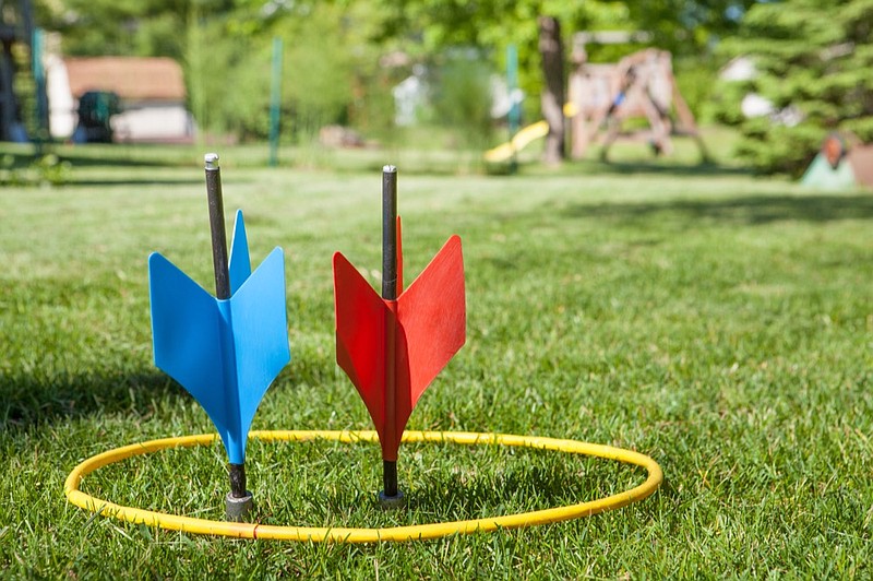a shot of some vintage lawn darts somtimes called JARTS. One of each color inside the yellow ring in a back yard setting. game tile / Getty Images
