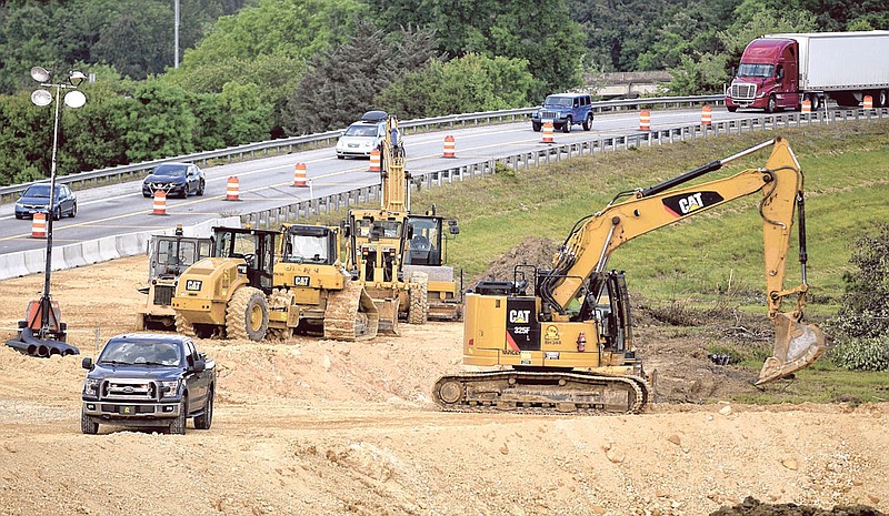 A Cat 325F hydraulic excavator, right, works last month on preparing the ground inside the split of Interstates 24 and 75. In the background, northbound I-75 traffic readies to merge into westbound I-24. In the far background, in the upper right, southbound I-75 traffic can be seen. (Staff Photo by Robin Rudd)