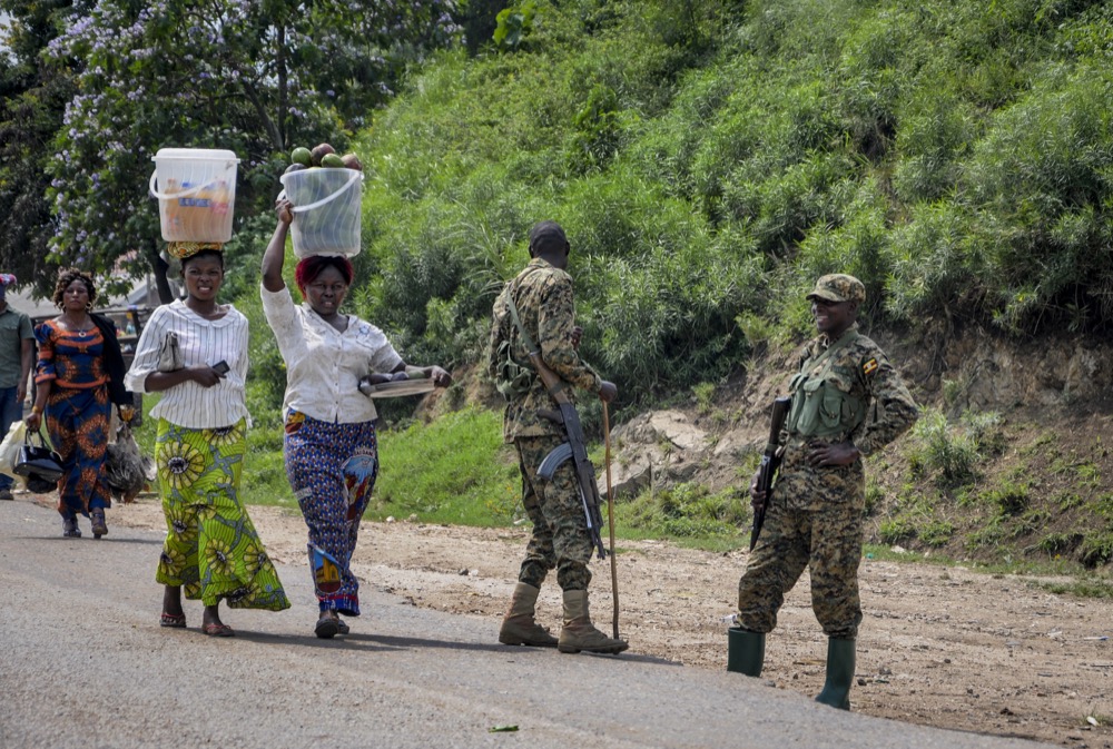 Two women heading towards Congo carry food on their heads as they walk past Ugandan army soldiers ensuring those crossing the border do not do so without being screened for symptoms of Ebola, at the Mpondwe border crossing to Congo, in western Uganda Friday, June 14, 2019. In Uganda, health workers had long prepared in case the Ebola virus got past the screening conducted at border posts with Congo and earlier this week it did, when a family exposed to Ebola while visiting Congo returned home on an unguarded footpath. (AP Photo/Ronald Kabuubi)