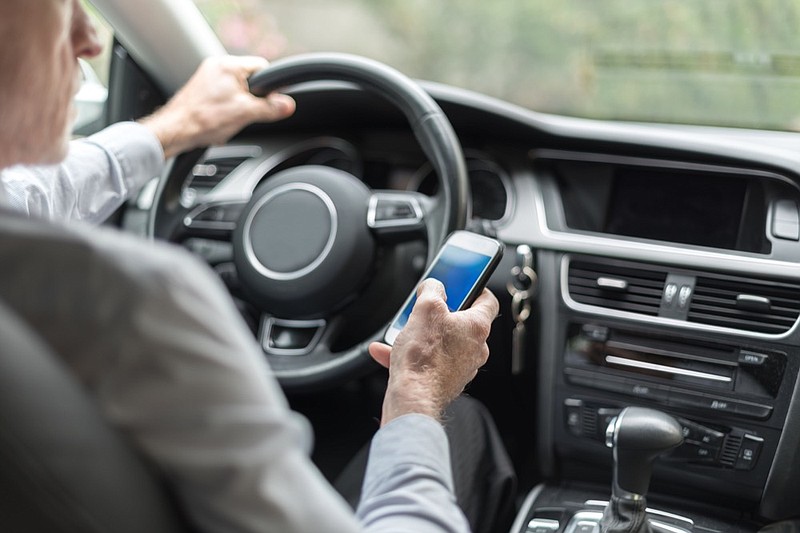 Man using a smartphone while driving a car phone tile phone driving tile / Getty Images