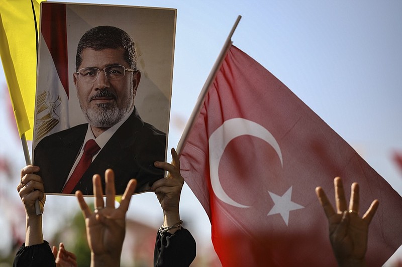 Supporters join Turkish President Recep Tayyip Erdogan, who attends funeral prayers in absentia for ousted former Egyptian President Mohammed Morsi, in poster, at Fatih Mosque in Istanbul, Tuesday, June 18, 2019. Funeral prayers were held in mosques across Turkey for Morsi, who had close ties to Erdogan. The former president, who was ousted by current President Abdel-Fattah el-Sissi in a military coup in 2013, collapsed in a courtroom in Egypt during trial on Monday and died. (AP Photo/Emrah Gurel)