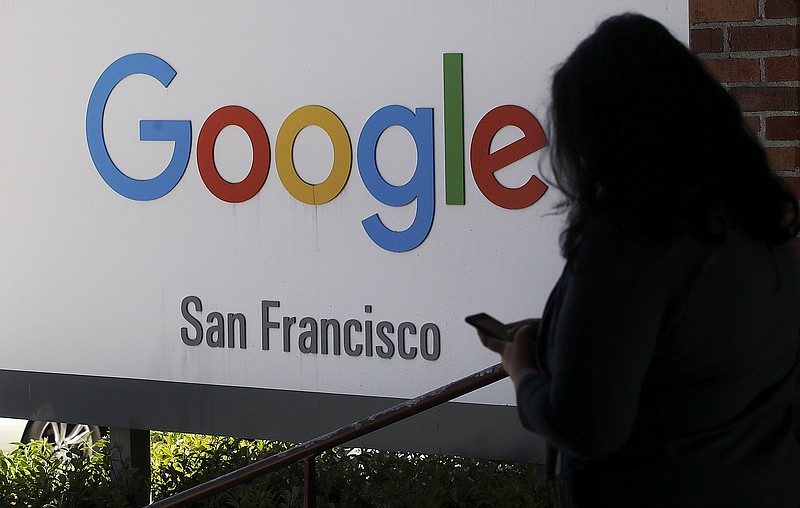 FILE - In this May 1, 2019, file photo, a woman walks past a Google sign in San Francisco. Google is making a $1 billion commitment to address the soaring price of housing in the San Francisco Bay Area, a problem that the internet company and its Silicon Valley peers helped create as the technology industry hired tens of thousands of high-paid workers.  (AP Photo/Jeff Chiu, File)