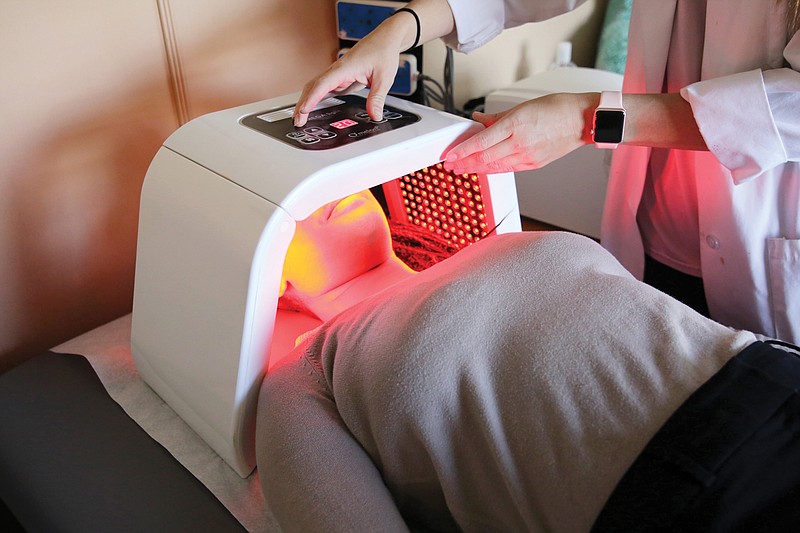 Monique Boyd, doctor's assistant, lies under the LED anti-aging facial rejuvenation machine as Kansas Carpenter, front desk manager, changes the settings to demonstrate how the machine works at the Chattanooga Wellness Natural Health Center Wednesday, May 15, 2019 in Chattanooga, Tennessee. 