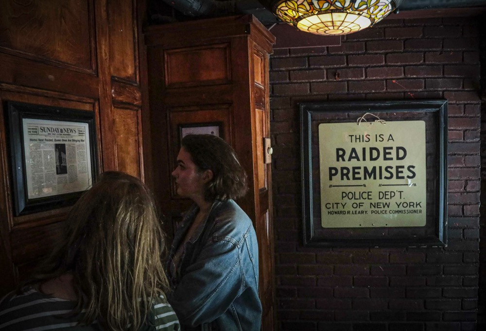 Stonewall Inn visitors read news clipping about the1969 riots that followed a police raid of a gay bar at the site, Friday June 14, 2019, in New York. Some of the coverage of rioting outside the gay bar, like the New York Daily News headlined a story "Homo Nest Raided, Queen Bees are Stinging Mad," was a source fury that led Stonewall to become a synonym for the fight for gay rights. (AP Photo/Bebeto Matthews)