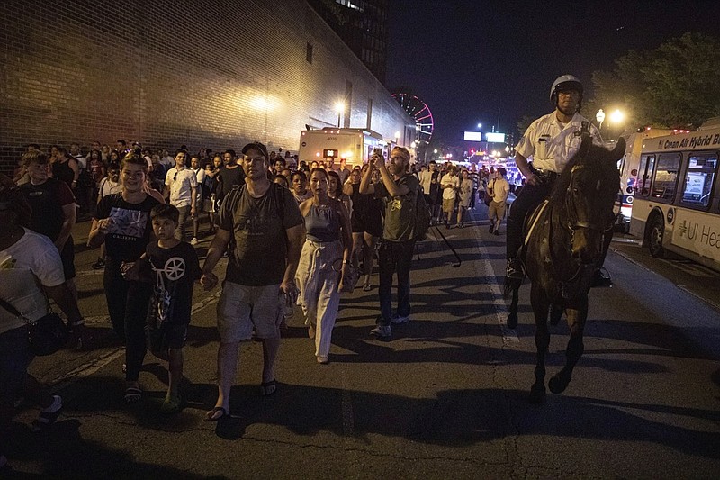 In this Thursday, July 4, 2019 photo, A Chicago Police Department (CPD) officer guard people as they stream out of Chicago's Navy Pier after reports of stabbings and threatening injuries after the 4th of July celebrations. Police said a false report of gunfire set off a stampede that trampled more than a dozen people. (AP Photo/Amr Alfiky)