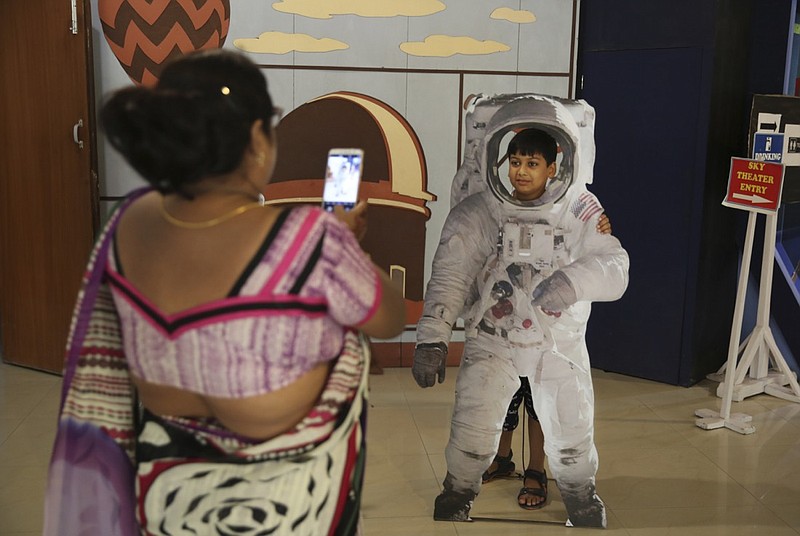 An Indian woman takes a photograph of her son as he poses in a cut-out of an astronaut at the Nehru Planetarium in New Delhi, India, Thursday, July 11, 2019. India is looking to take a giant leap in its space program and solidify its place among the world's spacefaring nations with its second unmanned mission to the moon, this one aimed at landing a rover near the unexplored south pole. (AP Photo/Altaf Qadri)