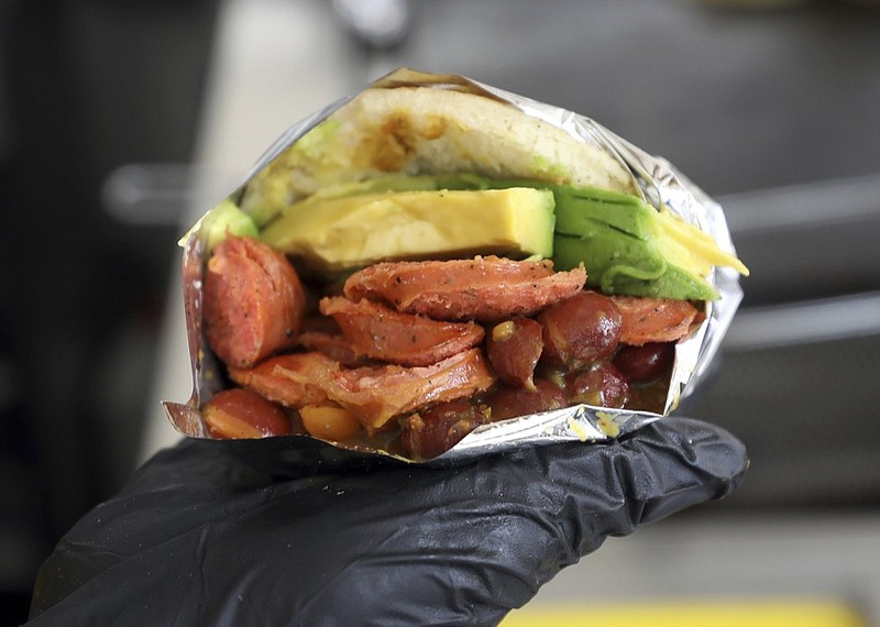In this June 11, 2019 photo, a food server shows a Venezuelan arepa made with Colombian ingredients at the "Arepas Cafe" fast food restaurant in Bogota, Colombia. Venezuelans like to jest that their beloved arepas are so widely consumed that babies come out of the womb with the corn flatbreads already in hand. Now, as millions flee their homeland's turmoil, they are taking Venezuela's most ubiquitous dish with them.(AP Photo/Fernando Vergara)
