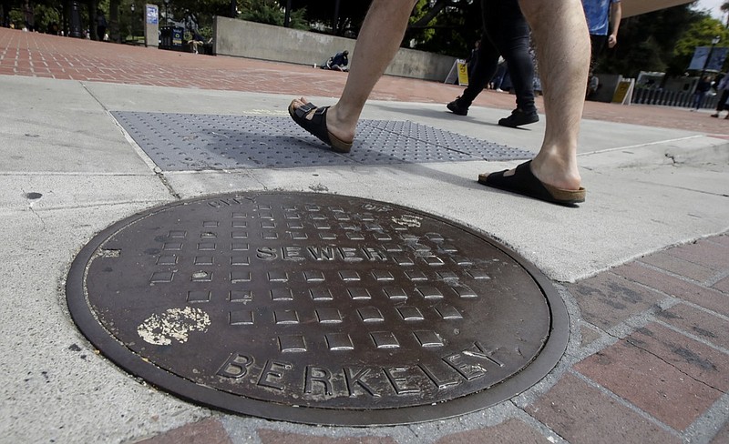 Pedestrians walk past a manhole cover for a sewer in Berkeley, Calif., Thursday, July 18, 2019. Soon students in Berkeley, California will have to pledge to "collegiate Greek system residences" instead of sororities or fraternities and city workers will have to refer to manholes as "maintenance holes." Officials in the liberal city this week passed an ordinance to replace some terms with gender-neutral words in the city code. (AP Photo/Jeff Chiu)