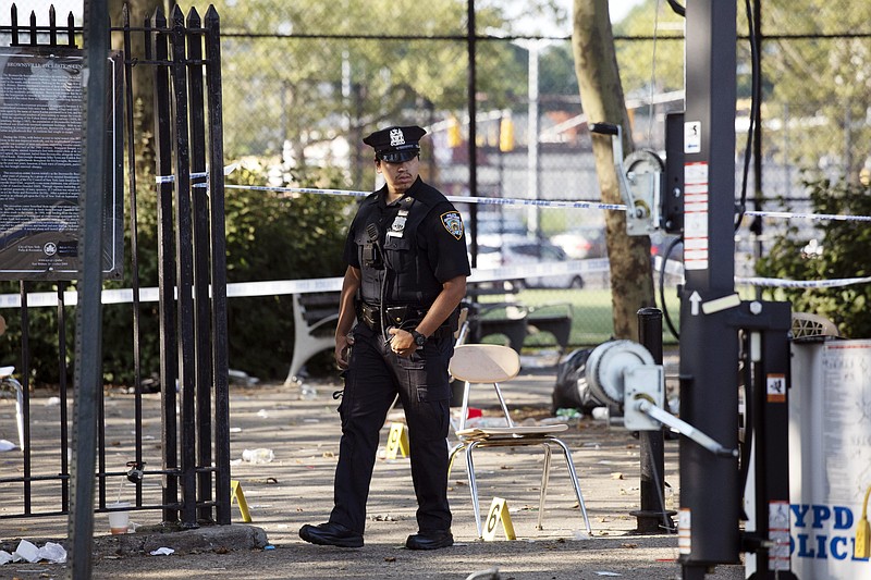 A police officer walks by yellow evidence markers at a playground in the Brownsville neighborhood in the Brooklyn borough of New York, Sunday, July 28, 2019. Police said, one man was killed and at least 11 others were injured in a shooting late Saturday night at the park. (AP Photo/Mark Lennihan)

