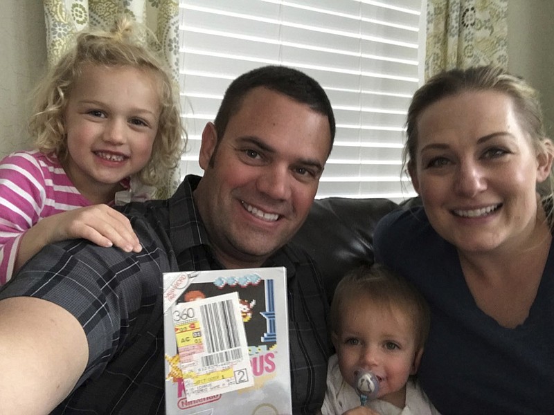 In this June 15, 2019 photo provided by Heritage Auctions, Scott Amos, along with his wife, Kristy, and daughters Grace, left, and Katie, pose in Reno, Nev., with an unopened copy of a 1987 cult-classic video game "Kid Icarus." The boxed game cartridge, still in the bag with the receipt for $38.45 from J.C. Penney's catalog department three decades earlier, is expected to sell for up to $10,000 at an online auction with Heritage Auctions. (Heritage Auctions via AP)
