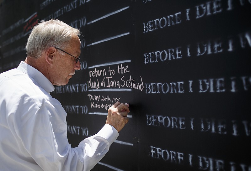 Keith Munford writes on a "Before I Die" art wall in Coolidge Park beneath the Chief John Ross Bridge on Tuesday, June 20, 2017, in Chattanooga, Tenn. The wall, sponsored by Hospice of Chattanooga, allows visitors to leave messages detailing what they want to do before they die. Staff photo by Doug Strickland 
