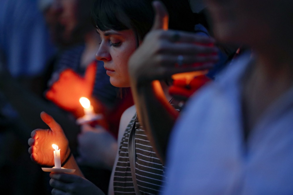 Mourners bow their heads in prayer as they gather for a vigil at the scene of a mass shooting, Sunday, Aug. 4, 2019, in Dayton, Ohio. Multiple people in Ohio have been killed in the second mass shooting in the U.S. in less than 24 hours, and the suspected shooter is also deceased, police said. (AP Photo/John Minchillo)