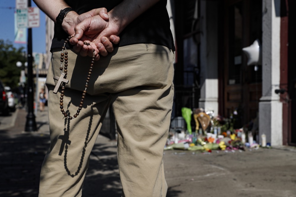 A mourner prays his rosary beads beside a memorial outside Ned Peppers bar that was the scene of a mass shooting the previous day, Monday, Aug. 5, 2019, in Dayton, Ohio. (AP Photo/John Minchillo)