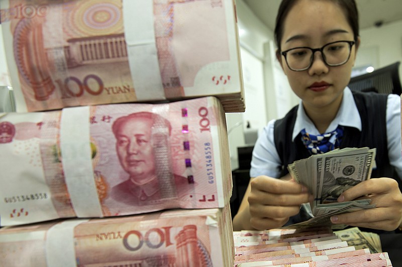 A bank employee counts U.S. dollar banknotes next to stack of 100 Chinese yuan notes at a bank outlet in Hai'an in eastern China's Jiangsu province, Tuesday, Aug. 6, 2019. China's yuan fell further Tuesday against the U.S. dollar, fueling fears about increasing global damage from Beijing's trade war with President Donald Trump. (Chinatopix via AP)