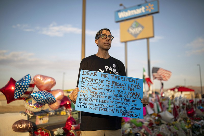 Rene Romo holds a sign bearing a message for President Donald Trump on Wednesday in El Paso, Texas. Rarely in recent memory has a relationship between a president and a city been so fraught, so as Trump arrived on Wednesday to try to meet the victims, protesters gathered at a memorial outside, many angry at the president's visit. (Ivan Pierre Aguirre/The New York Times)