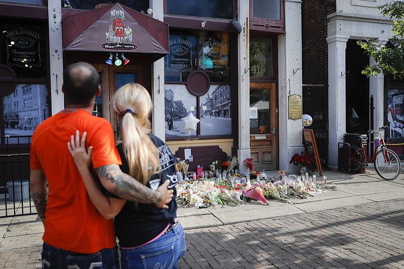 In this Aug. 6, 2019, file photo, mourners pause at a makeshift memorial for the slain and injured outside Ned Peppers bar in the Oregon District after a mass shooting that occurred early Sunday morning in Dayton. Annette Gibson Strong started placing candles at a makeshift memorial the day of the shooting on Sunday. Strong says she's continued to care for the memorial near Ned Peppers Bar in Dayton. It was outside the bar that Dayton police shot and killed the shooter as he approached the bar's entrance.(AP Photo/John Minchillo, File)