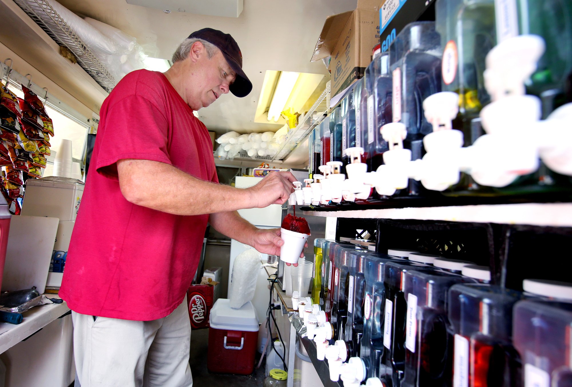 Staff photo by Erin O. Smith / Bill Henderson, the owner of Bill's Shaved Ice, makes a cherry shaved ice for a customer Monday, August 12, 2019 at Coolidge Park in Chattanooga, Tennessee. Henderson has been in business for about 18 years from about March through October. Henderson said as long as the fountain in Coolidge Park draws out crowds to cool off and have fun, he has a pretty good crowd of customers. The heat index on Tuesday is forecast to be over 100.