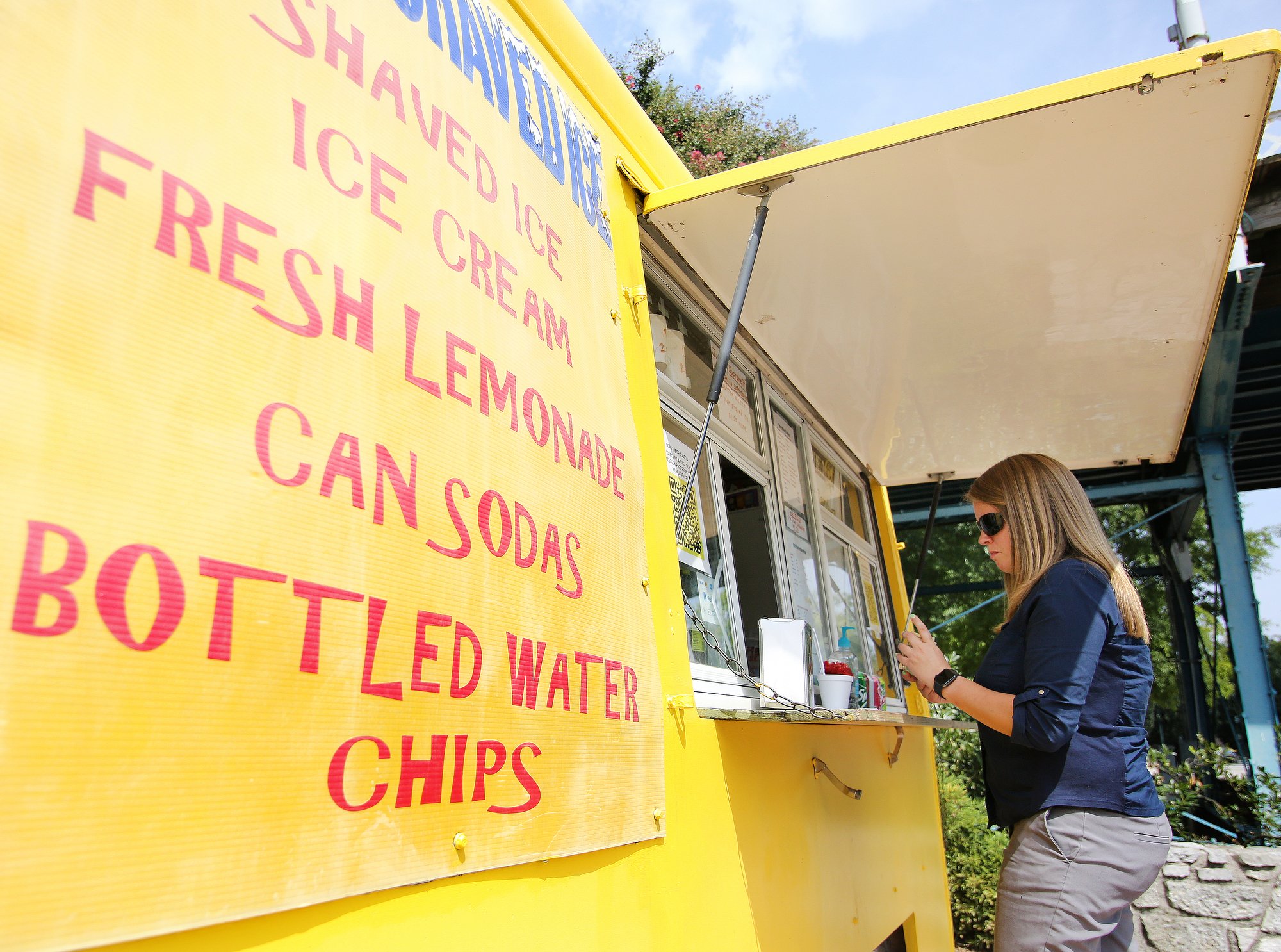 Staff photo by Erin O. Smith / Emily Huckstep stops by Bill's Shaved Ice for a treat after an interview Monday, August 12, 2019 at Coolidge Park in Chattanooga, Tennessee. The owner of Bill's Shaved Ice, Bill Henderson, says that he sees the most customers when locals brings their kids to the fountain in Coolidge Park to cool off. The heat index on Tuesday is forecast to be over 100.