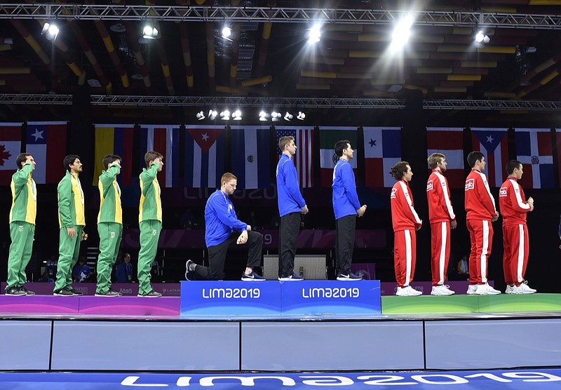 In this Friday, Aug. 9, 2019 photo, released by Lima 2019 News Services, Race Imboden of the United States takes a knee, as teammates Mick Itkin and Gerek Meinhardt stand on the podium after winning the gold medal in team's foil, at the Pan American Games in Lima, Peru. "Racism, gun control, mistreatment of immigrants, and a president who spreads hate are at the top of a long list" of America's problems, Imboden said in a tweet sent after his medals ceremony. "I chose to sacrifice my moment today at the top of the podium to call attention to issues that I believe need to be addressed. (Jose Sotomayor/Lima 2019 News Services via AP)