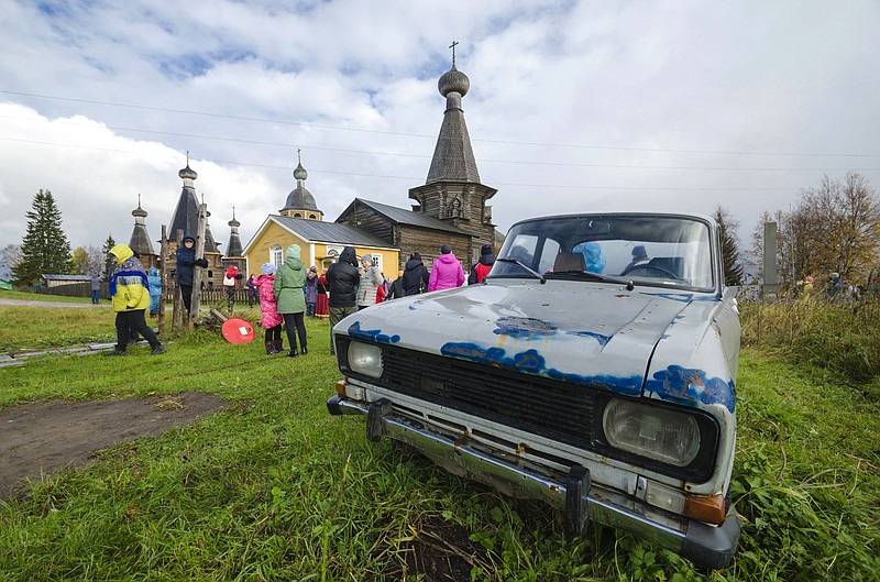 People walk the street on Oct. 7, 2018, with the 18th century Trinity Church in the background in the village of Nyonoksa, northwestern Russia.